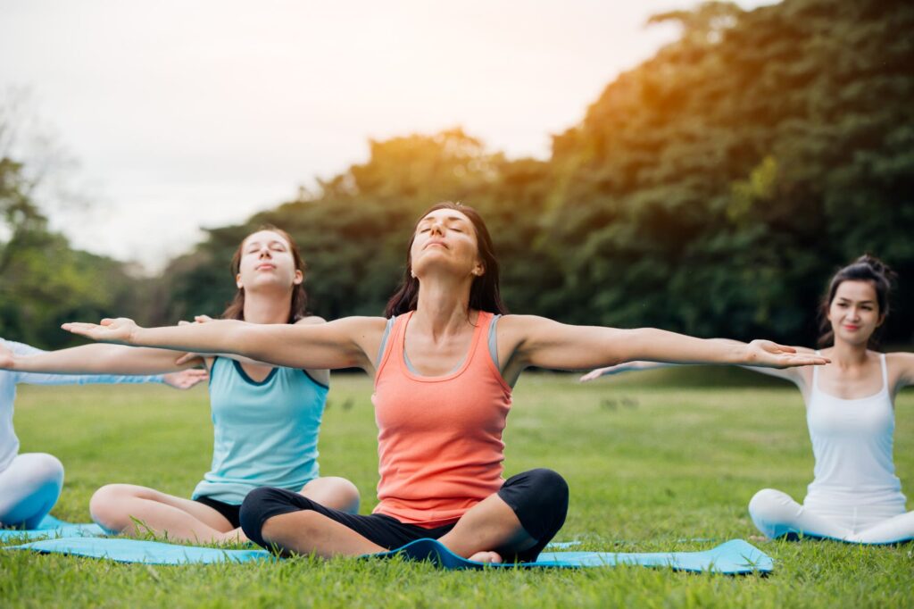 Two women practicing outdoor yoga with open arms.