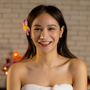 Smiling woman with a flower in her hair and a towel wrapped around her.