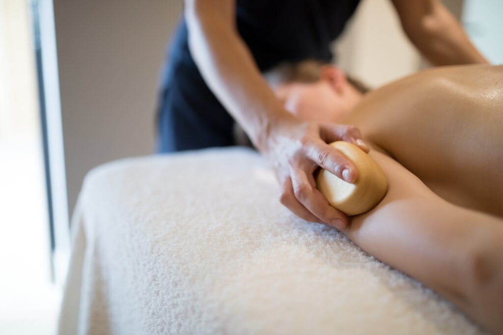 Massage therapist using wooden tool to massage patient