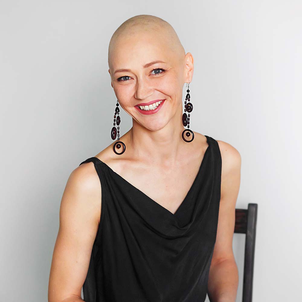 Smiling bald woman in a black sleeveless top and statement earrings.
