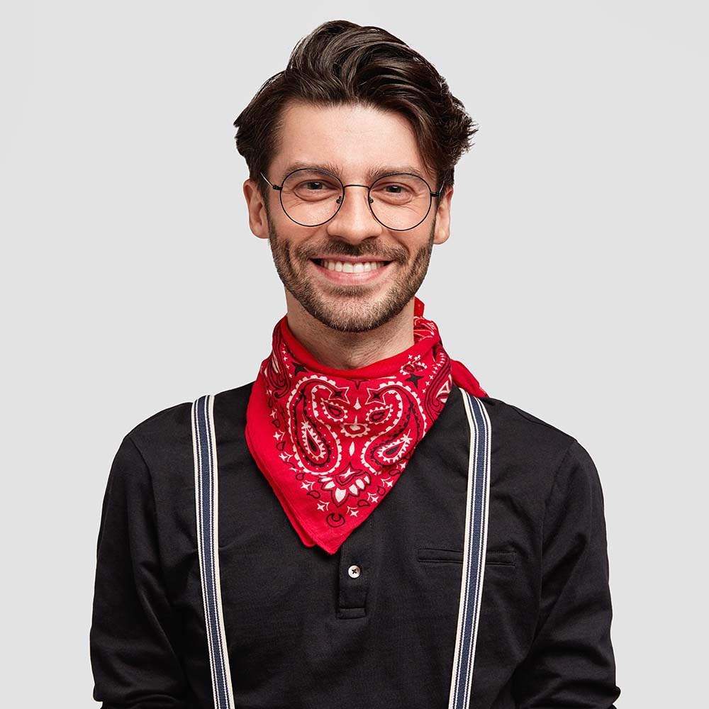 Smiling man wearing glasses, a red bandana, and suspenders over a black shirt.