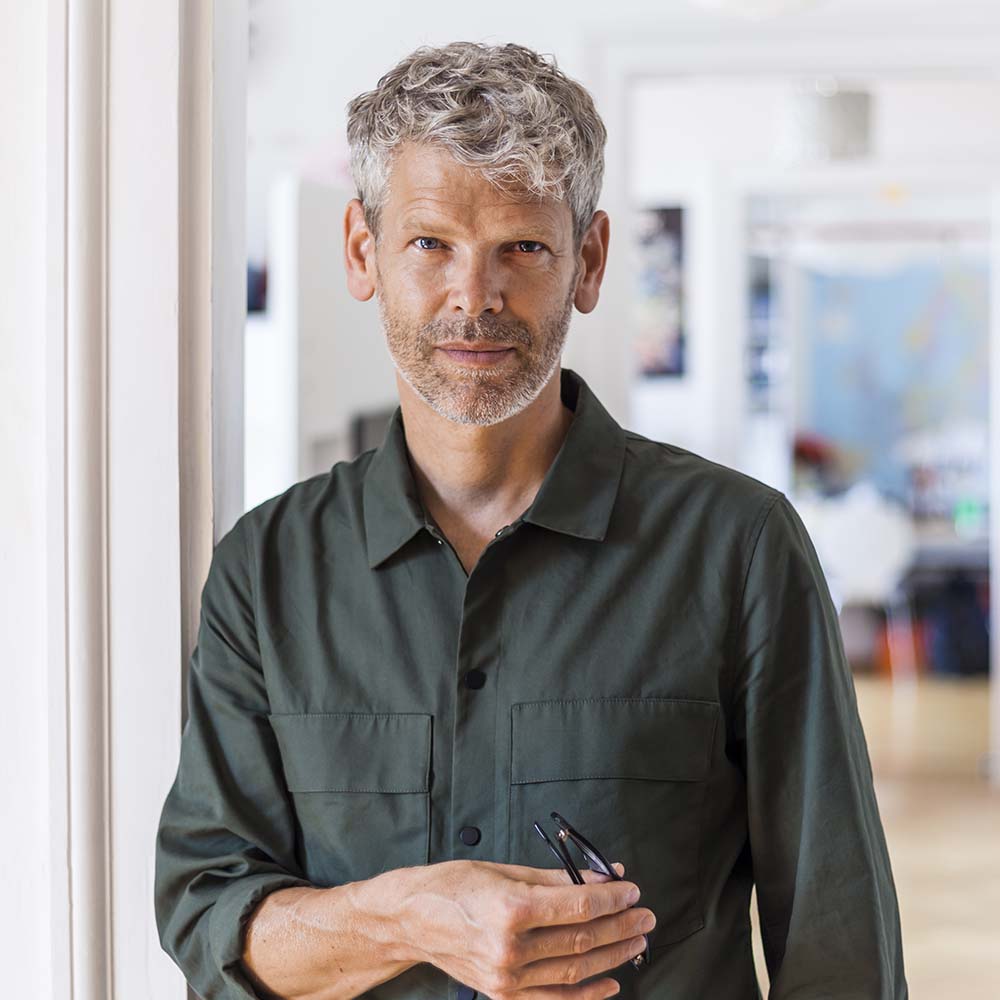 A man with gray hair and beard wearing a dark green shirt.