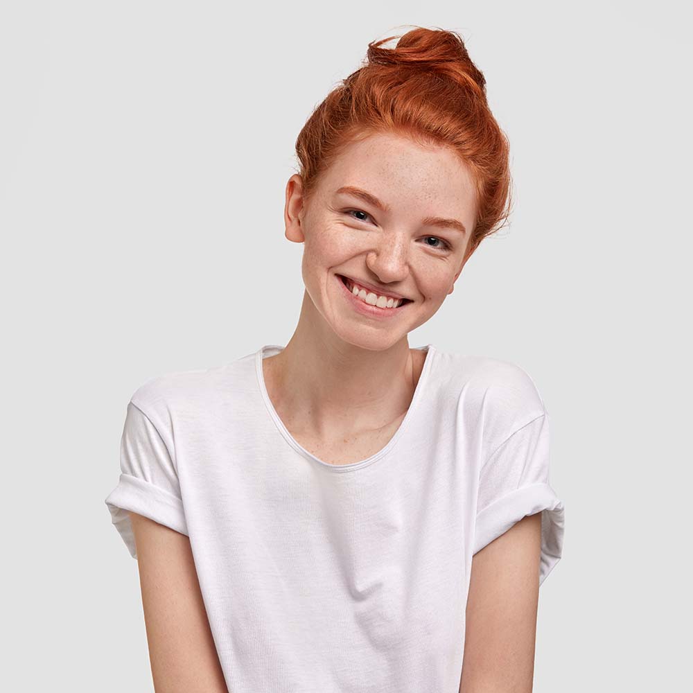 Smiling young woman with red hair in a white t-shirt against a plain background.