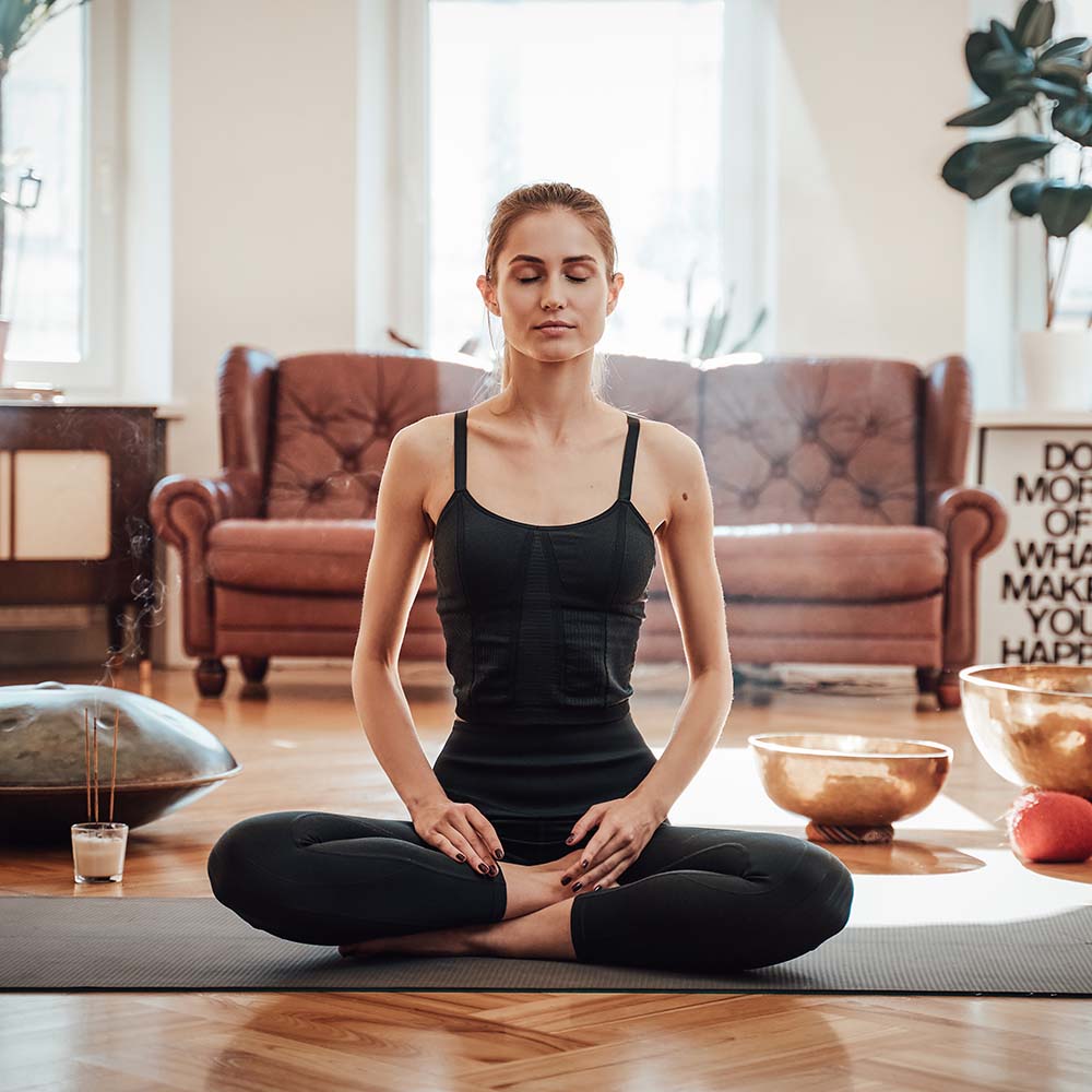 Woman meditating in a serene living room with natural light.