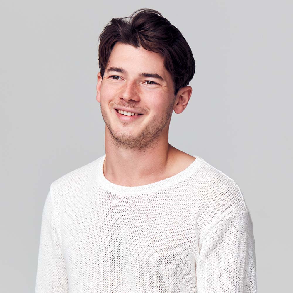 Smiling young man in a white sweater against a plain background.
