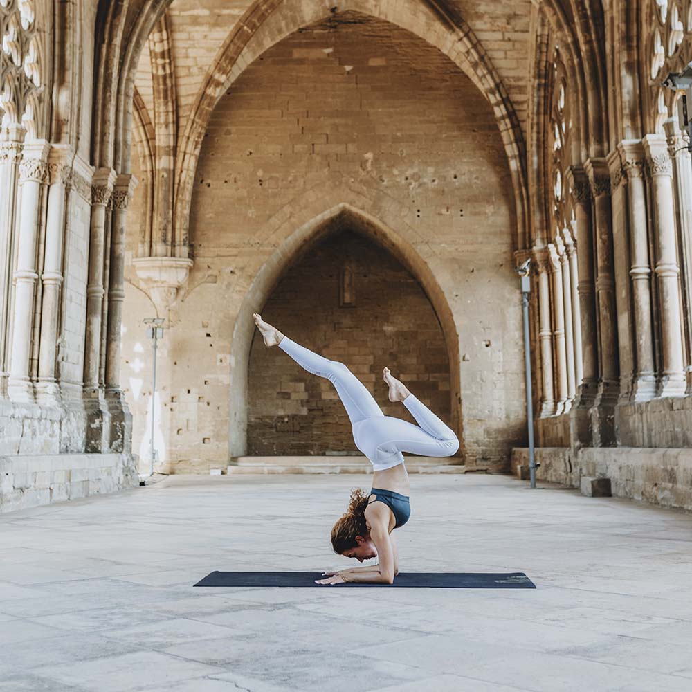 A person practices yoga in a historic arched stone hall.