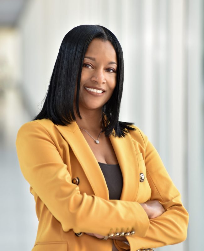 Confident woman in a yellow blazer smiling with arms crossed.